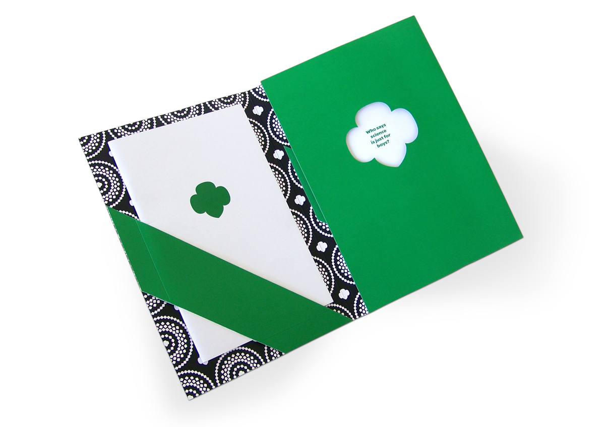 GIRL SCOUTS CASE STATEMENT<br><br>The folder opens to reveal a fireworks of trefoils, and pockets designed to mimic the iconic Girl Scouts sash. House in this first pocket is a book containing the general case for Girl Scouts. Facing that is a trefoil die-cut whose window previews case-making with much greater specificity. Sitting across a table from Jane Goodall? Let’s talk to her directly through this window.